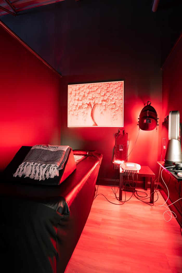 The red light therapy room, lit red, with the treatment bed and a folded Red Light Method throw.