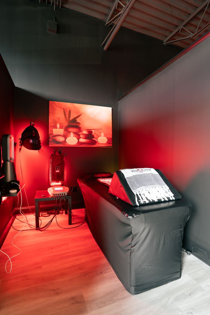 The red light therapy room from the doorway, the bed made up under the red glow.