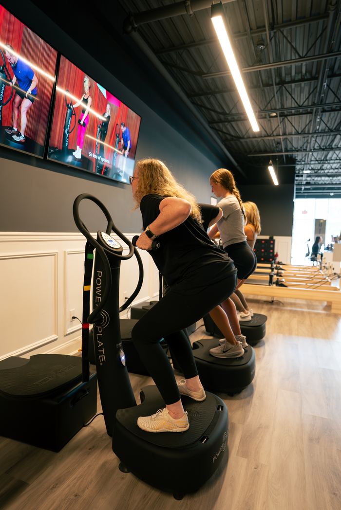 Members side by side on the Power Plates, working through the class together.